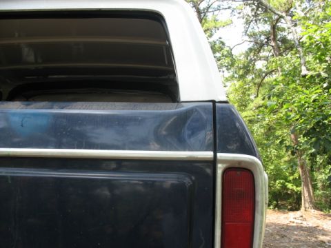 1978 Ford Bronco - Close-up of the rear passenger side of a 1978 Ford Bronco, showing a dented panel and a red taillight.