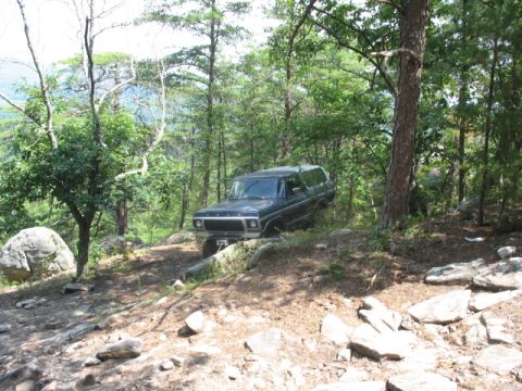 1978 Ford Bronco - A dark blue 1978 Ford Bronco navigates a rocky, wooded terrain.
