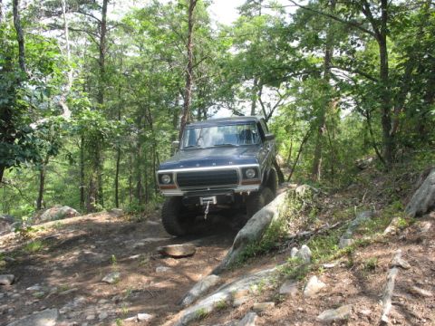 1978 Ford Bronco - A dark blue 1978 Ford Bronco navigates a challenging, rocky path through a dense forest.
