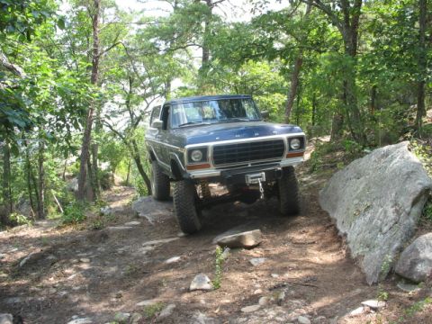1978 Ford Bronco - Blue 1978 Ford Bronco tackling an off-road trail in a wooded area.