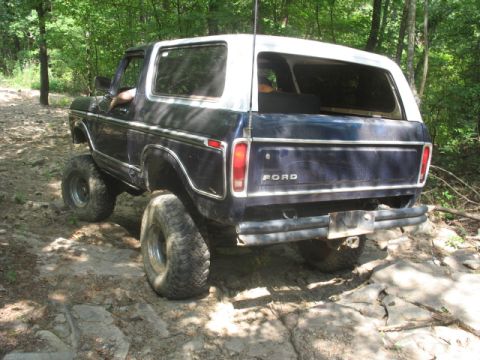 1978 Ford Bronco - Rear view of a 1978 Ford Bronco with a white top, navigating a rocky off-road path.