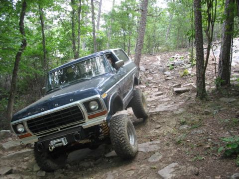 1978 Ford Bronco - A dark blue 1978 Ford Bronco navigates a challenging, rocky path through a dense forest.