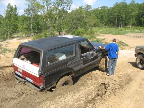 1978 Ford Bronco - A person watches as a black Ford Bronco gets stuck in thick mud off-road.