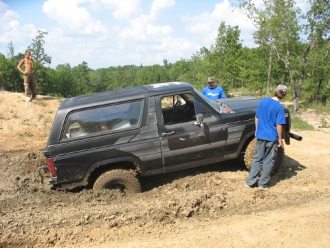 1978 Ford Bronco - A black SUV is stuck in the mud with three people observing the situation.