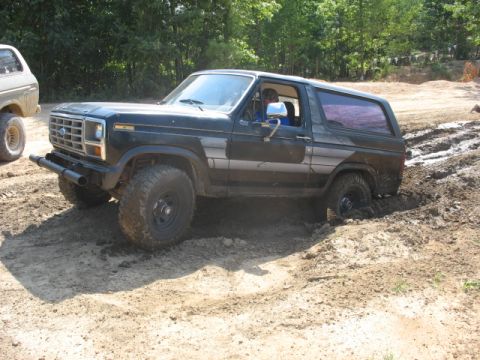 1978 Ford Bronco - A dark 1978 Ford Bronco navigates a muddy off-road course, with another vehicle visible in the background.