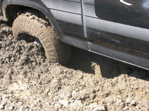1978 Ford Bronco - Vehicle stuck in mud, only side panel and tire visible.