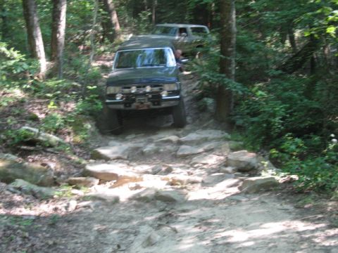 1978 Ford Bronco - Two 4x4 vehicles tackle a challenging rocky path through a wooded area.