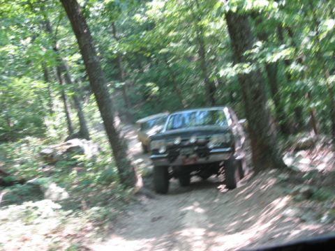 1978 Ford Bronco - Two SUVs navigate a dusty trail surrounded by trees and rocks.