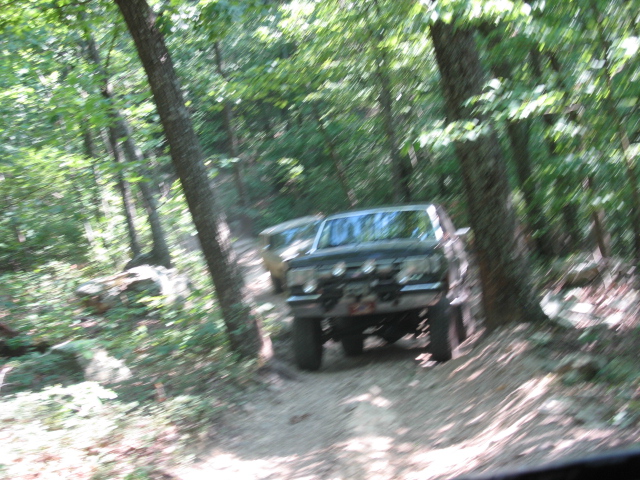Two off-road vehicles driving on a dirt path through a wooded area