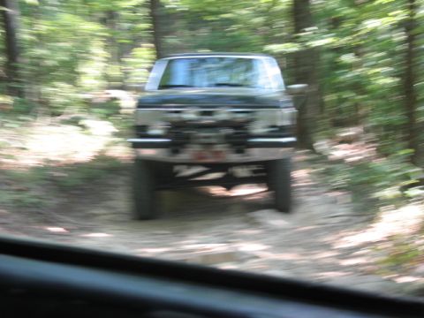 1978 Ford Bronco - A dark SUV navigates a wooded trail, its motion blurred by the camera's movement.