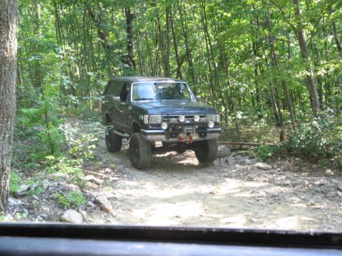 1978 Ford Bronco - A modified SUV navigates a wooded trail, its large tires kicking up dust on the rocky path.