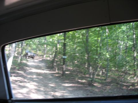 1978 Ford Bronco - View of an off-road vehicle traveling on a dirt path surrounded by trees.