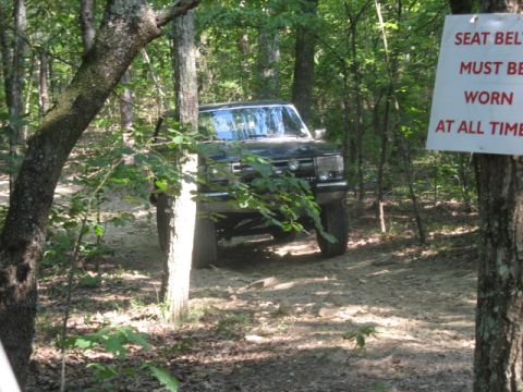 1978 Ford Bronco - 1978 Ford Bronco navigating a rough trail in a wooded area. A sign reminds visitors to wear seat belts.
