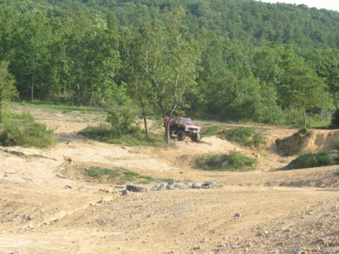 1978 Ford Bronco - A red off-road SUV navigates a challenging dirt track amidst a wooded, hilly landscape.