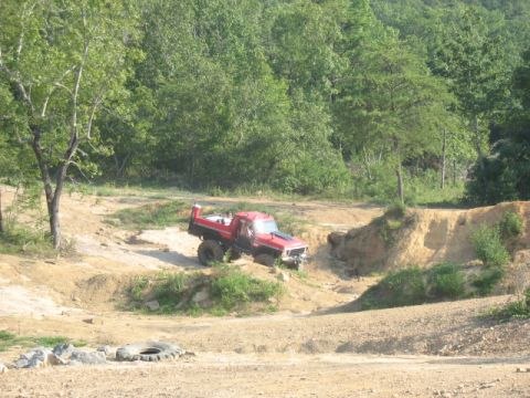 1978 Ford Bronco - A modified red truck tackles a challenging off-road course amidst wooded terrain.