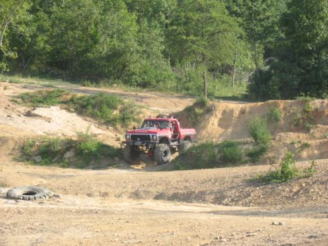 1978 Ford Bronco - A modified red pickup truck navigates a challenging off-road course with steep dirt inclines.