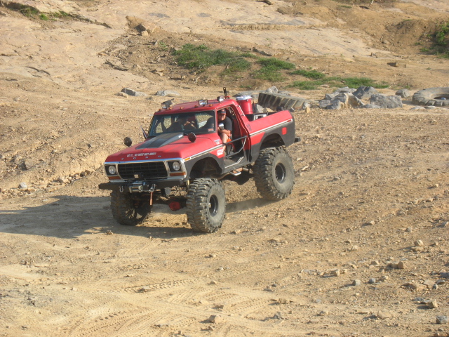 red 1978 Ford Bronco with large tires driving on a dirt trail