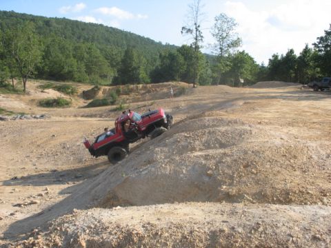1978 Ford Bronco - A red pickup truck navigates a steep dirt incline in an off-road park.