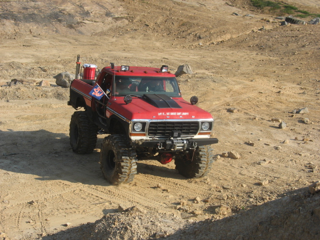 Red 1978 Ford Bronco lifted with large tires, driving on a dirt track