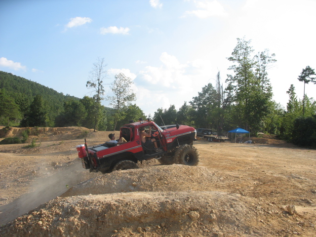 Red 1978 Ford Bronco driving on dirt mound, kicking up dust
