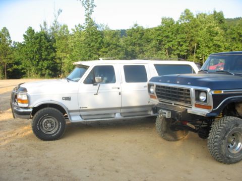 1978 Ford Bronco - Two Ford trucks are parked side-by-side on a dirt lot with trees in the background.