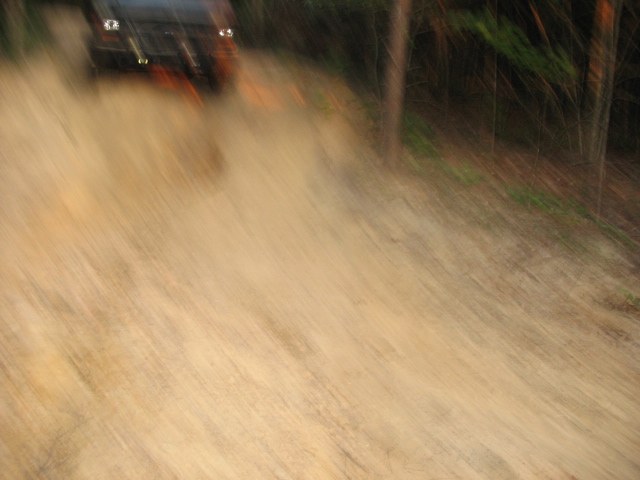 Off-road vehicle driving on a dirt path, kicking up dust. Trees visible in the background