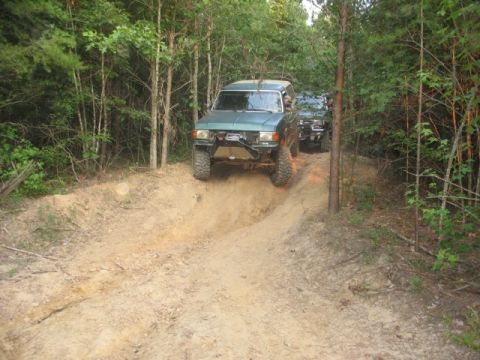 1978 Ford Bronco - Two off-road SUVs navigate a steep dirt path through a wooded area.