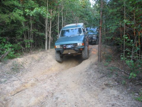 1978 Ford Bronco - Two SUVs navigate a challenging off-road trail through a wooded area.
