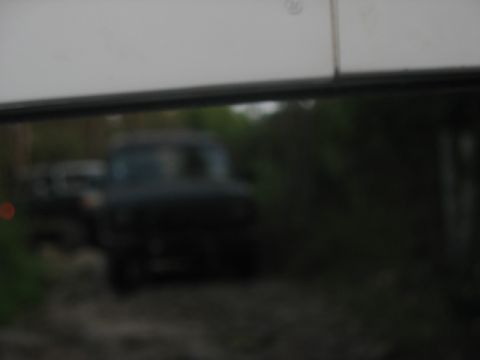 1978 Ford Bronco - A dark colored truck is visible through a window, partially obscured and out of focus.