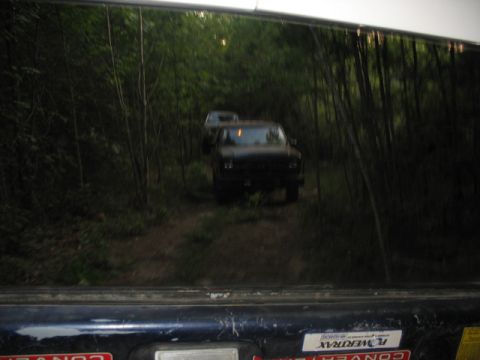 1978 Ford Bronco - A reflection shows two trucks on a wooded path, with one vehicle following the other.
