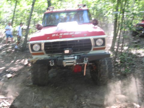 1978 Ford Bronco - This modified truck is navigating a wooded trail, with dust billowing from its tires.