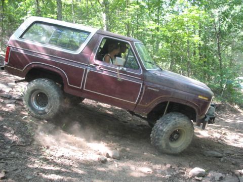 1978 Ford Bronco - A maroon 1978 Ford Bronco with a white top navigates a dirt trail off-road.