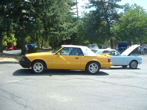 1999 Ford Crown Victoria - A yellow convertible car is parked next to a light blue coupe at an outdoor car show.