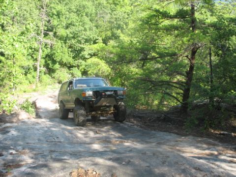 1978 Ford Bronco - This modified SUV navigates a challenging rocky trail surrounded by dense forest.