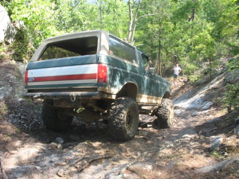 1978 Ford Bronco - Green Ford Bronco navigates a challenging rocky trail in a wooded area.