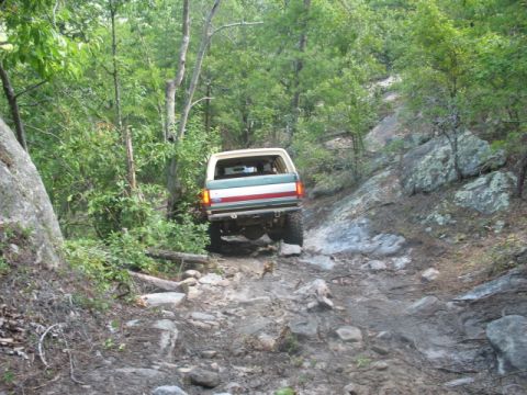 1978 Ford Bronco - A Ford Bronco navigates a challenging, rocky path through a dense forest.