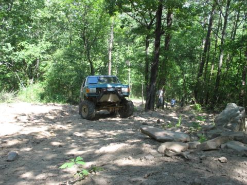 1978 Ford Bronco - Modified off-road SUV navigates a wooded trail with large tires and a prominent front bumper.