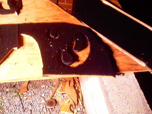 Close-up of a car trunk's interior, showing a wooden panel with a black felt cutout in the shape of a stylized creature or symbol