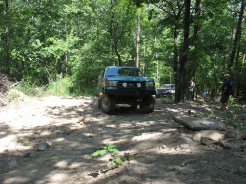 1978 Ford Bronco - A lifted green truck navigates a wooded trail with another vehicle visible in the background.