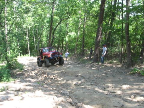 1978 Ford Bronco - A red Jeep Wrangler navigates a challenging off-road course through a dense forest.
