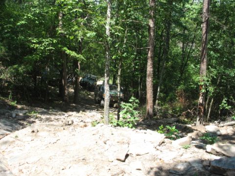 1978 Ford Bronco - Multiple off-road vehicles navigate a challenging, wooded trail with rocky terrain.