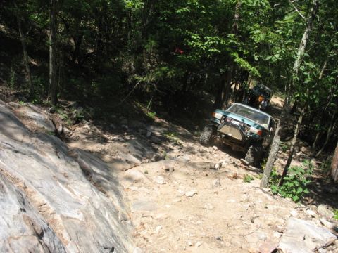 1978 Ford Bronco - Two off-road vehicles navigate a steep, rocky trail through a dense forest.