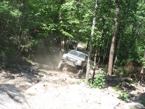 1978 Ford Bronco - Off-road vehicles navigate a challenging, dusty trail through a wooded area.