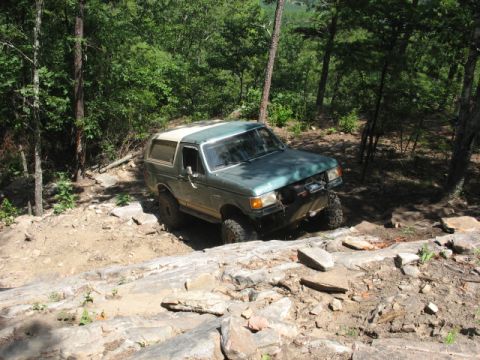 1978 Ford Bronco - A green Ford Bronco with a white top is shown off-roading on a challenging rocky path.