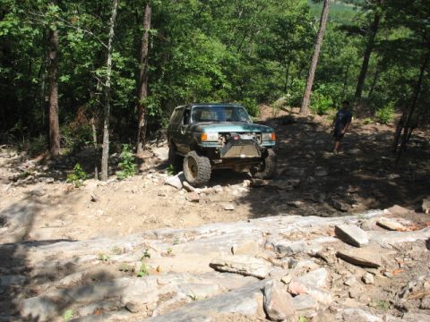 1978 Ford Bronco - An off-road SUV navigates a challenging rocky trail in a wooded area.