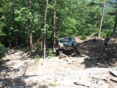 1978 Ford Bronco - Off-road vehicle tackling a challenging rocky path surrounded by trees.