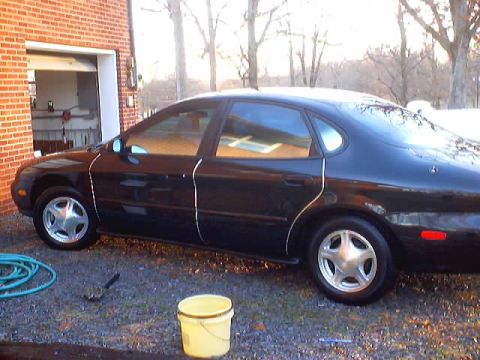 1999 Ford Taurus - A black 1999 Ford Taurus sedan is parked next to a brick garage.