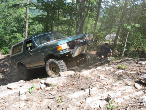 1978 Ford Bronco - An off-road SUV navigates a challenging rocky trail with a person observing nearby.