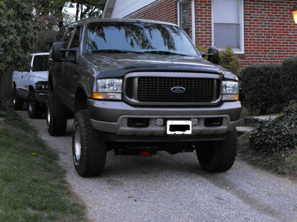 Gray lifted Ford Excursion SUV parked in driveway, front three-quarter view with large tires.