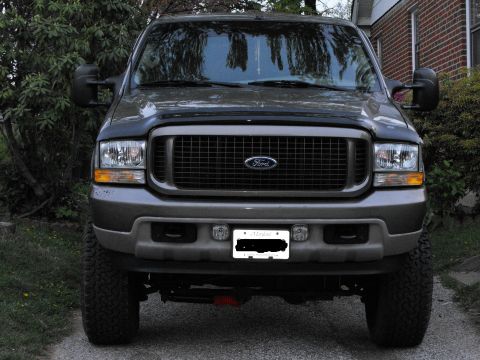 2003 Ford Excursion - This large SUV is parked in front of a brick house with trees in the background.